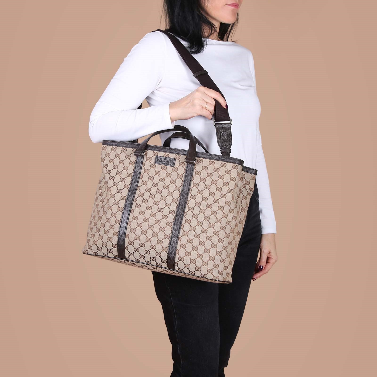 Woman wearing beige GG monogram canvas tote bag with brown leather trim and adjustable shoulder strap — Gucci | Endless UAE