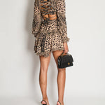 Rear view of woman wearing brown leopard print dress with ruched cutout back detail, long sleeves, and ruffled hem, paired with black heels and handbag — Zimmermann | Endless UAE