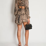 Rear view of woman wearing brown leopard print dress with ruched cutout back detail, long sleeves, and ruffled hem, paired with black heels and handbag — Zimmermann | Endless UAE