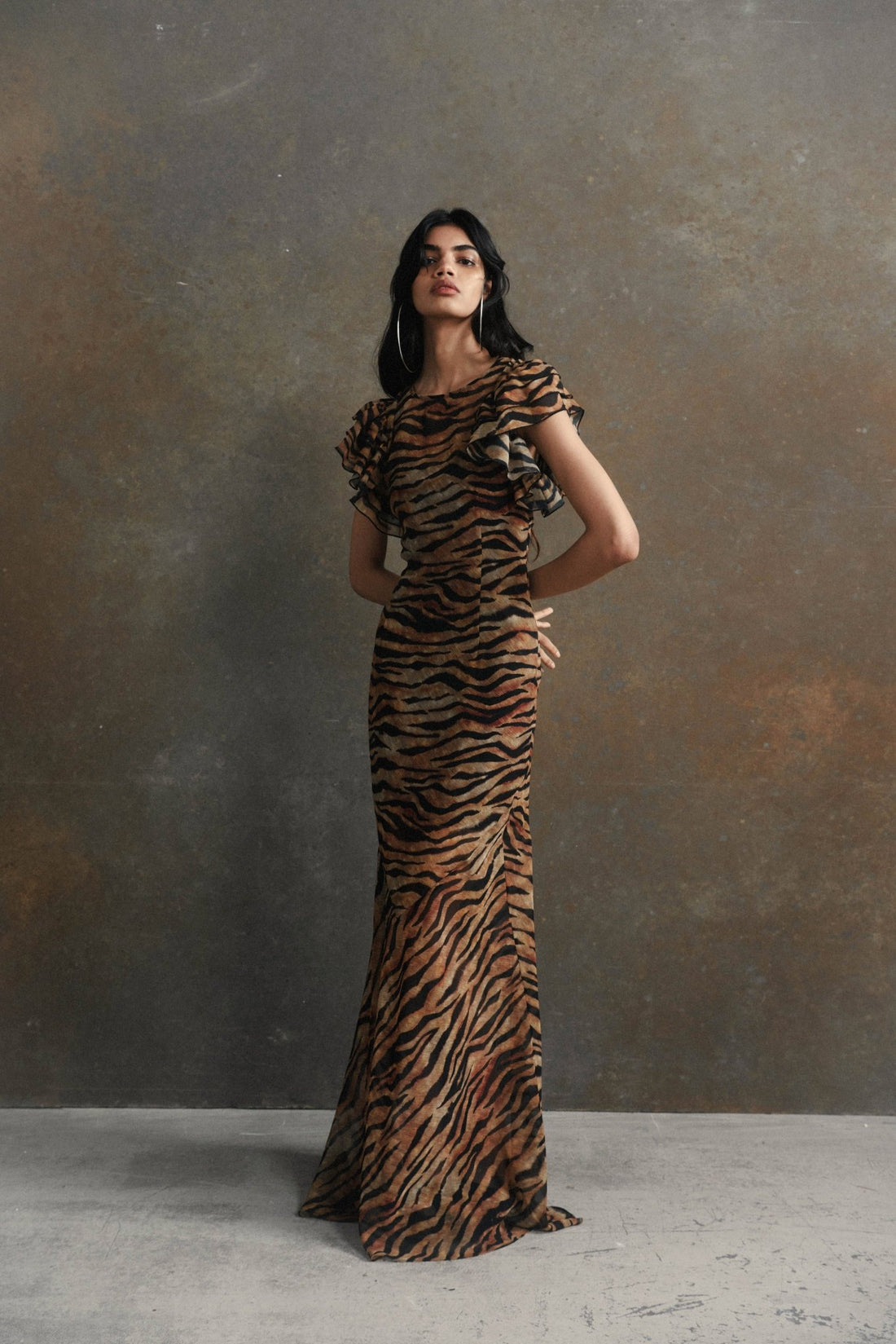 Woman wearing tiger stripe maxi dress with short puffed sleeves against textured background — De La Vali | Endless UAE