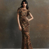 Woman wearing tiger stripe maxi dress with short puffed sleeves against textured background — De La Vali | Endless UAE