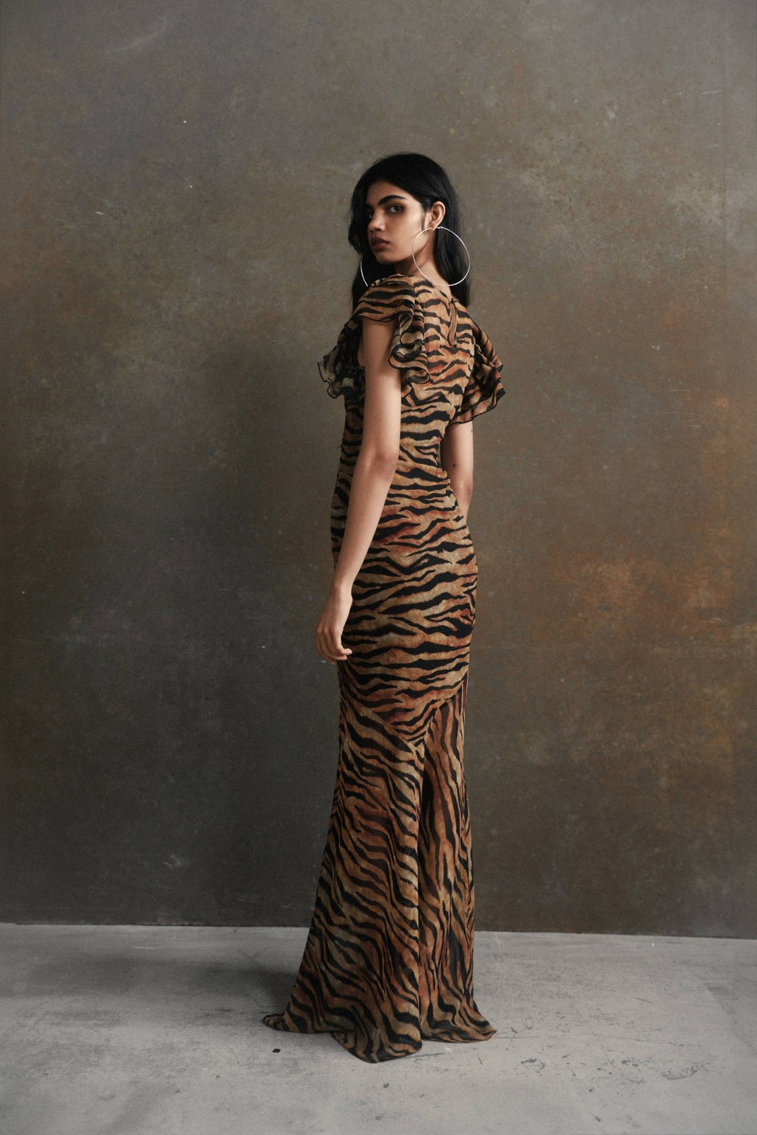 Woman wearing tiger stripe maxi dress with short puffed sleeves against textured background — De La Vali | Endless UAE