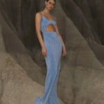 Blue sequined maxi dress with asymmetric cutout detail and thin straps on model against rock formation — Baobab | Endless UAE