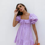 Lilac linen mini dress with puff sleeves and smocked bodice, styled with sunglasses and orange Fanta bottles — Else Adelia | Endless UAE