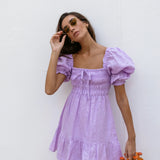 Lilac linen mini dress with puff sleeves and smocked bodice, styled with sunglasses and orange Fanta bottles — Else Adelia | Endless UAE