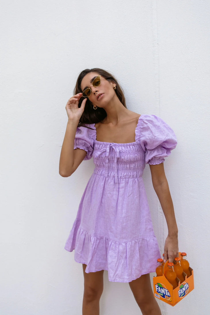 Lilac linen mini dress with puff sleeves and smocked bodice, styled with sunglasses and orange Fanta bottles — Else Adelia | Endless UAE