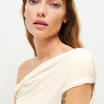 Woman wearing cream off-shoulder Cello Knit Top with black denim skirt and nude heels — Reformation | Endless UAE