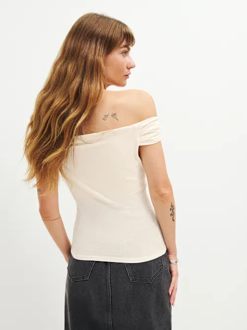Woman wearing cream off-shoulder Cello Knit Top with black denim skirt and nude heels — Reformation | Endless UAE