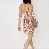 Woman wearing white mini dress with red floral print, chain strap detail, and white sneakers, shown from back — Reformation | Endless UAE