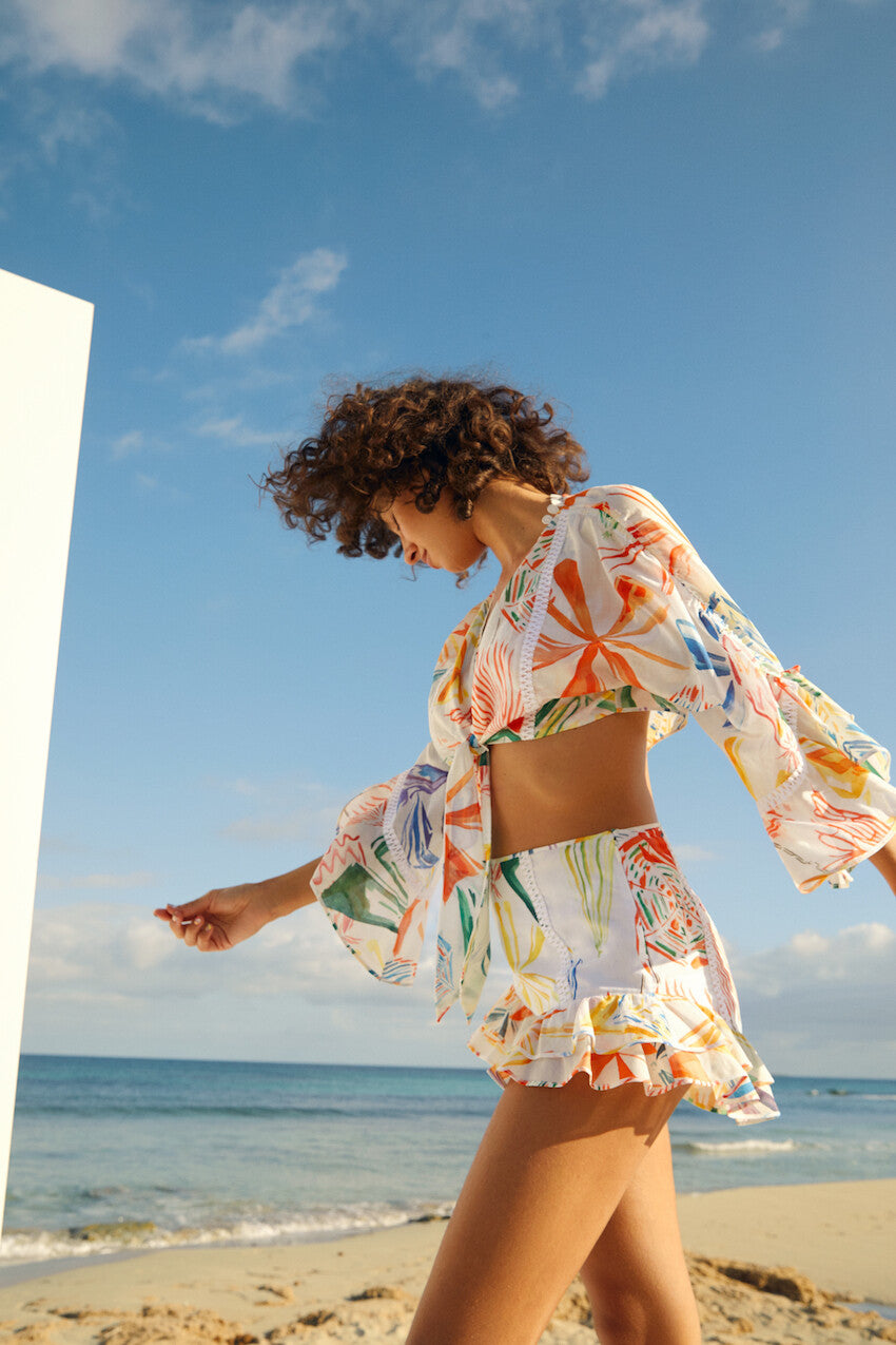 Woman wearing colorful printed crop top and shorts beach co-ord set with bell sleeves by the ocean — Charo Ruiz Ibiza | Endless UAE