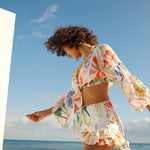 Woman wearing colorful printed crop top and shorts beach co-ord set with bell sleeves by the ocean — Charo Ruiz Ibiza | Endless UAE