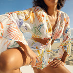Woman wearing a colorful tropical print two-piece set with pom-pom trim on beach — Charo Ruiz Ibiza | Endless UAE