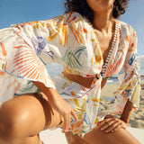 Woman wearing a colorful tropical print two-piece set with pom-pom trim on beach — Charo Ruiz Ibiza | Endless UAE