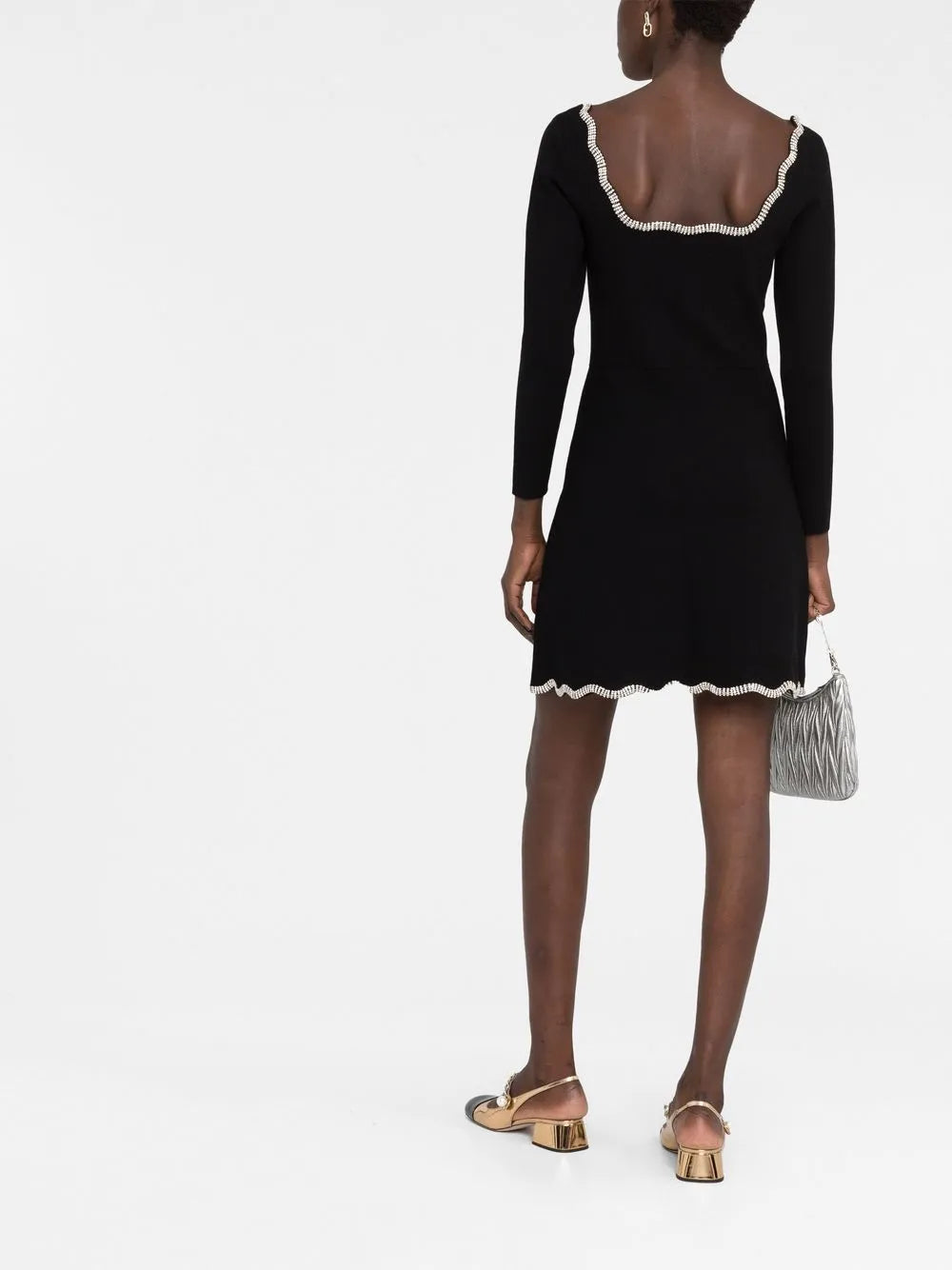 Woman wearing black long-sleeve mini dress with white crystal-embellished trim at neckline and hem, paired with gold metallic sandals — Sandro | Endless UAE