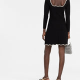 Woman wearing black long-sleeve mini dress with white crystal-embellished trim at neckline and hem, paired with gold metallic sandals — Sandro | Endless UAE