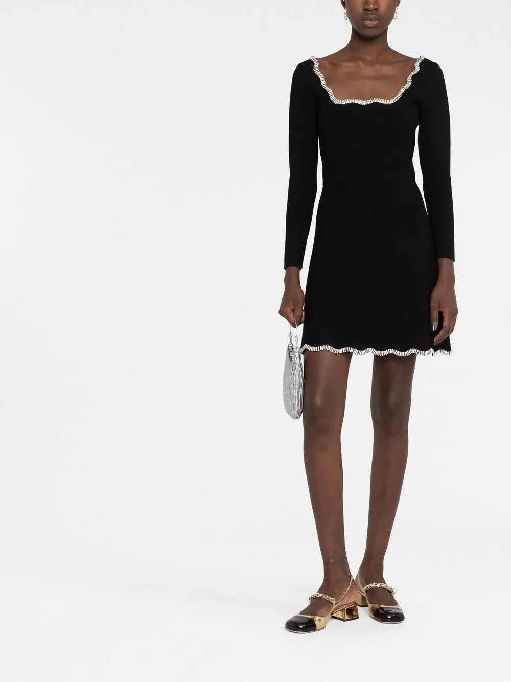 Black long-sleeve mini dress with white crystal-embellished scalloped trim at neckline and hem, modeled with metallic shoes and silver clutch — Sandro | Endless UAE