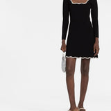 Black long-sleeve mini dress with white crystal-embellished scalloped trim at neckline and hem, modeled with metallic shoes and silver clutch — Sandro | Endless UAE