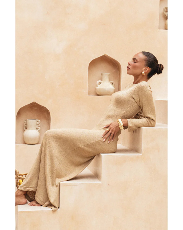 Woman wearing beige long-sleeve maxi dress standing in minimalist architectural setting — Miharo | Endless UAE