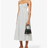 Woman wearing white midi dress with black polka dots, thin straps, and fitted bodice paired with black kitten heels — Reformation | Endless UAE