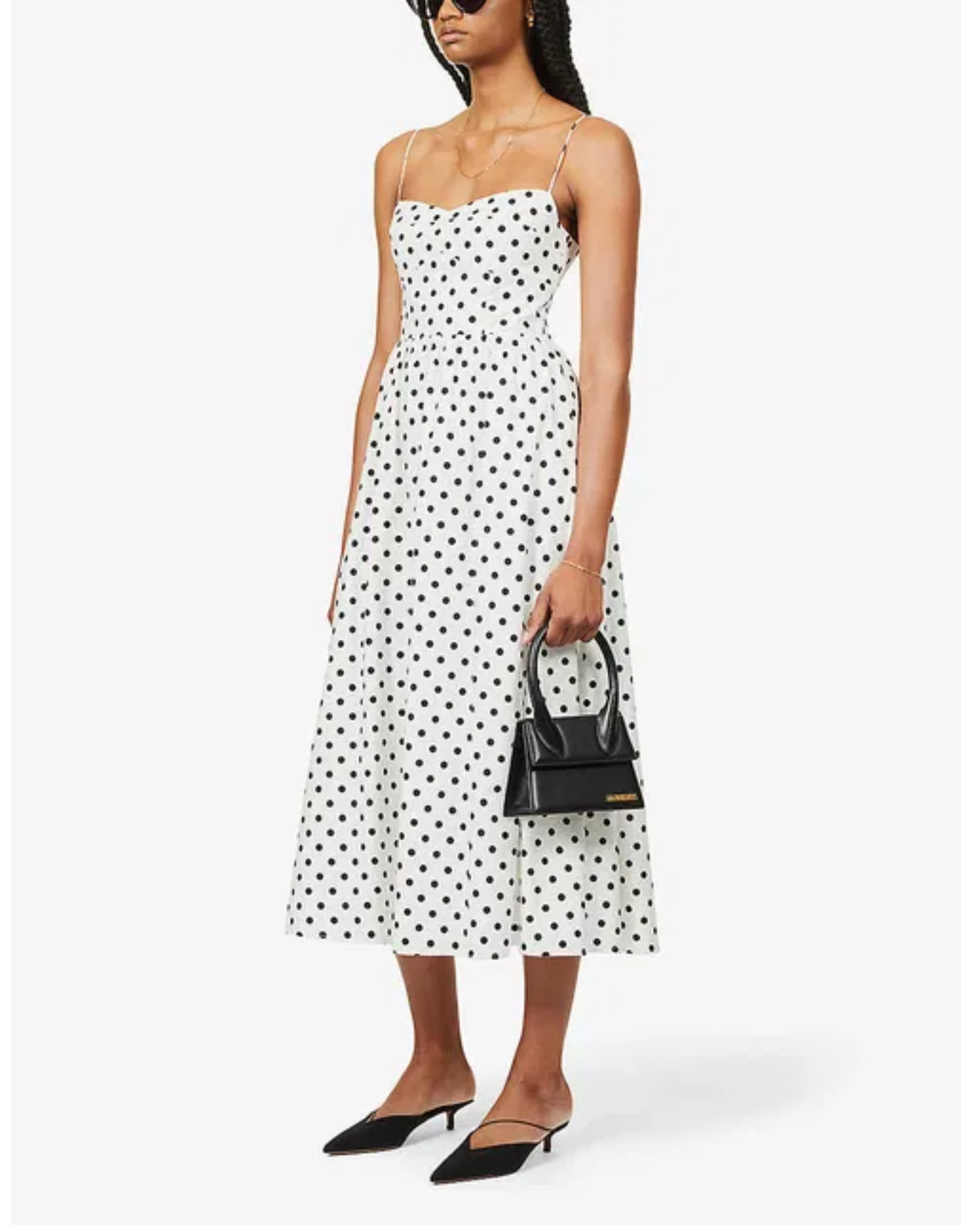 Woman wearing white midi dress with black polka dots, thin straps, and fitted bodice paired with black kitten heels — Reformation | Endless UAE
