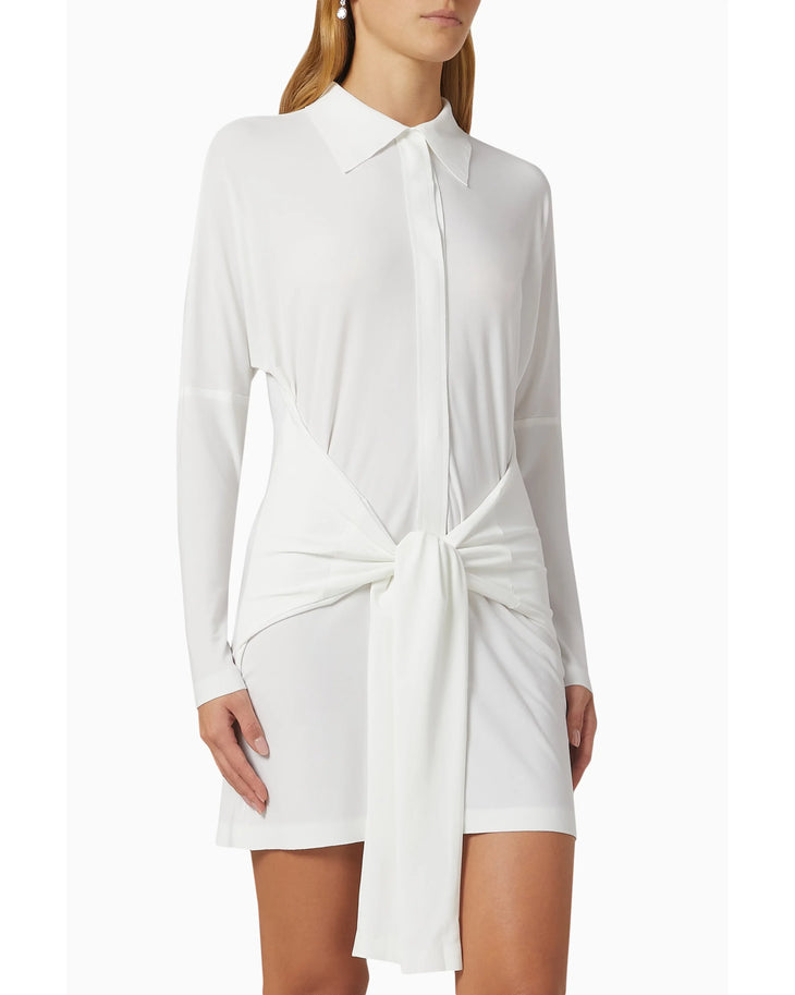 Woman wearing white long-sleeve shirt dress with front tie detail and white slide sandals — Norma Kamali | Endless UAE