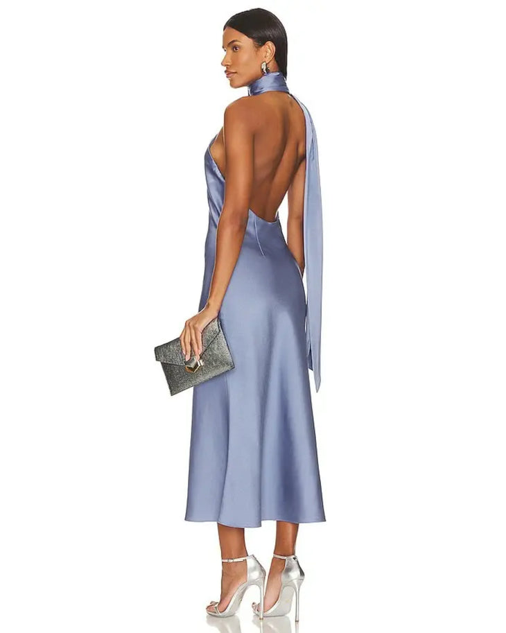 Periwinkle blue satin midi dress with open back and halter neck tie detail, worn with silver heels and clutch — Misha | Endless UAE