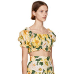 Model wearing yellow floral print crop top and matching skirt set with green leaves on beige background — Dolce and Gabbana | Endless UAE