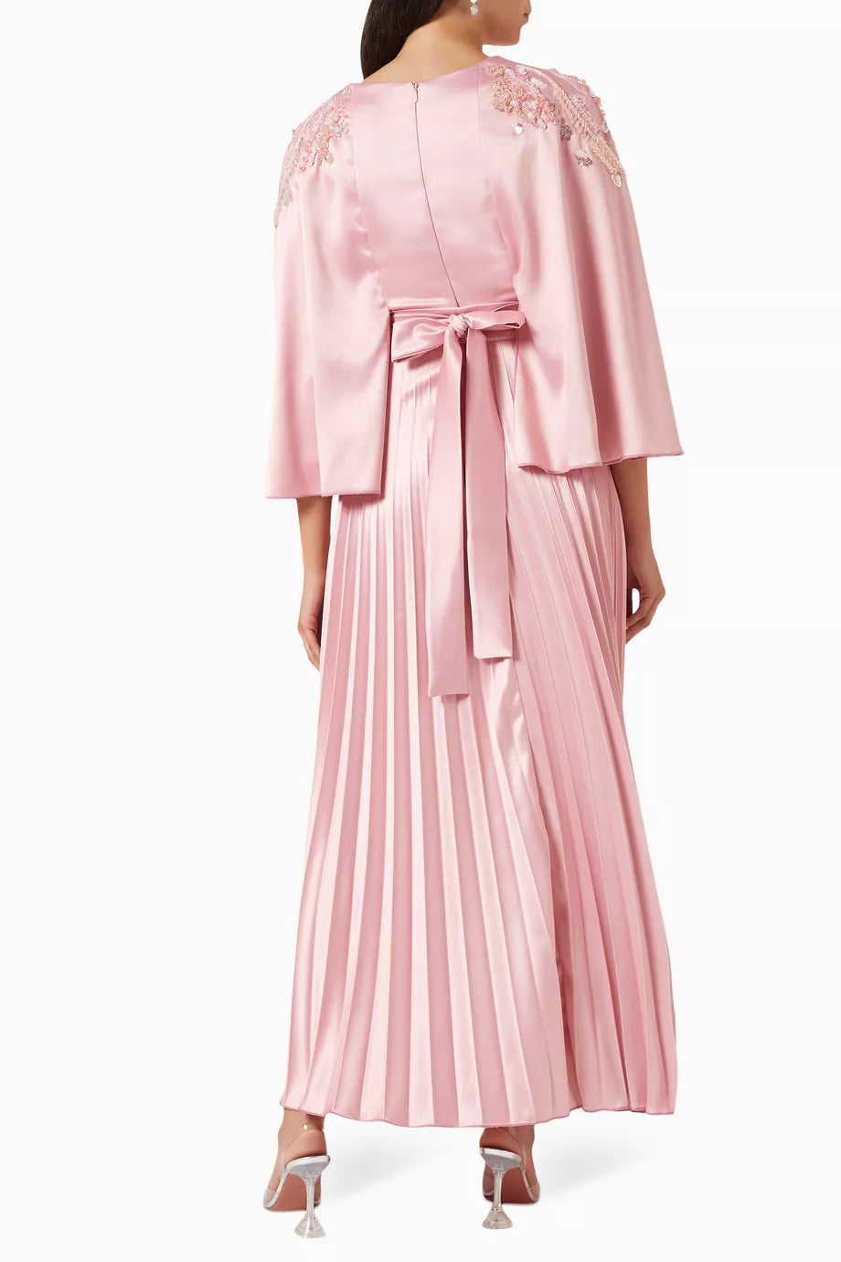 Woman wearing a pink satin pleated dress with matching cape overlay and metallic heels — Nass | Endless UAE