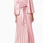 Woman wearing a pink satin pleated dress with matching cape overlay and metallic heels — Nass | Endless UAE