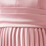 Woman wearing a pink satin pleated dress with matching cape overlay and metallic heels — Nass | Endless UAE