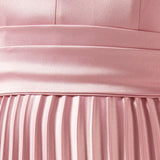 Woman wearing a pink satin pleated dress with matching cape overlay and metallic heels — Nass | Endless UAE