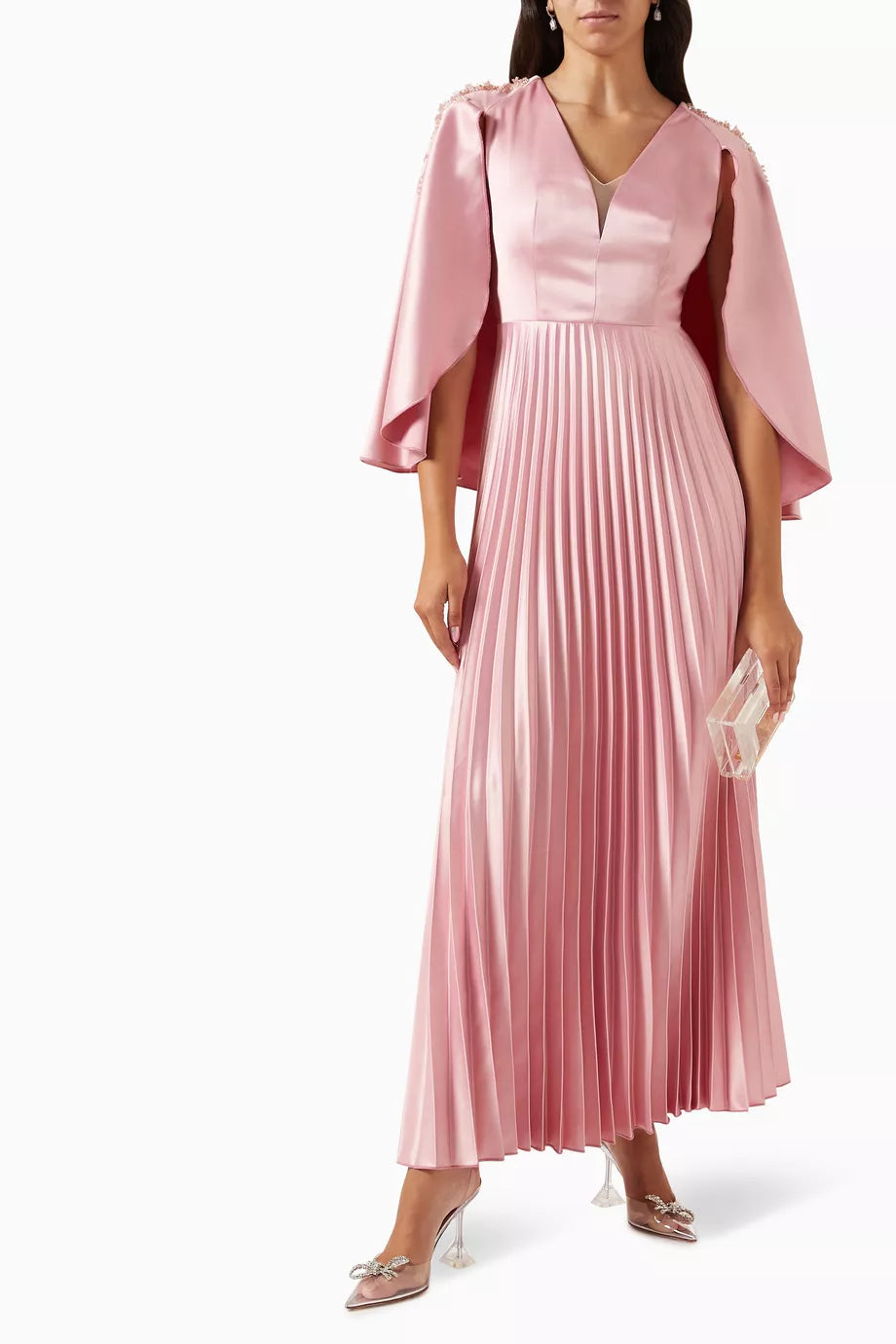 Woman wearing a pink satin pleated dress with matching cape overlay and metallic heels — Nass | Endless UAE