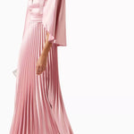 Woman wearing a pink satin pleated dress with matching cape overlay and metallic heels — Nass | Endless UAE
