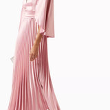 Woman wearing a pink satin pleated dress with matching cape overlay and metallic heels — Nass | Endless UAE