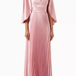 Woman wearing a pink satin pleated dress with matching cape overlay and metallic heels — Nass | Endless UAE