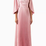 Woman wearing a pink satin pleated dress with matching cape overlay and metallic heels — Nass | Endless UAE
