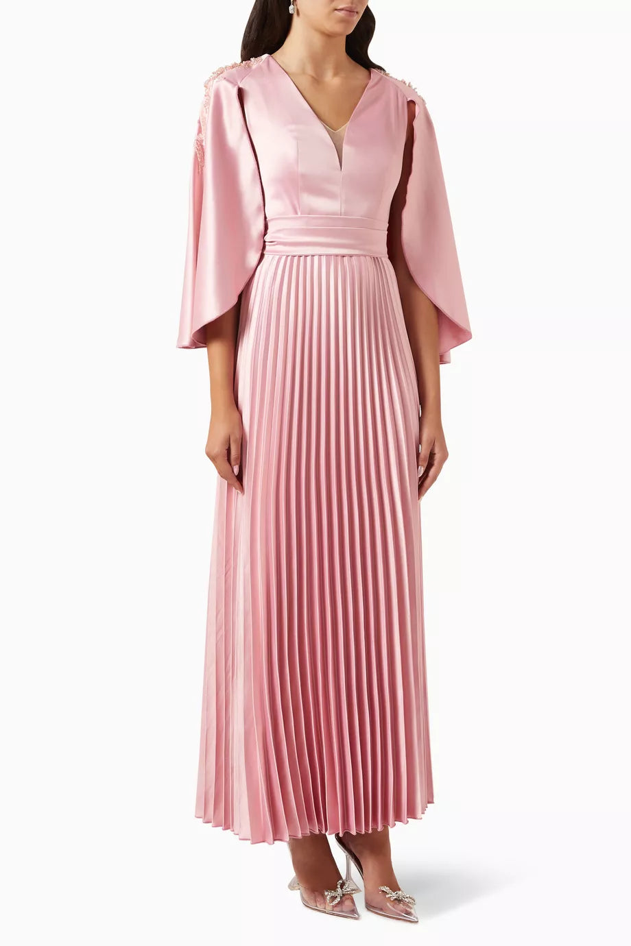Woman wearing a pink satin pleated dress with matching cape overlay and metallic heels — Nass | Endless UAE