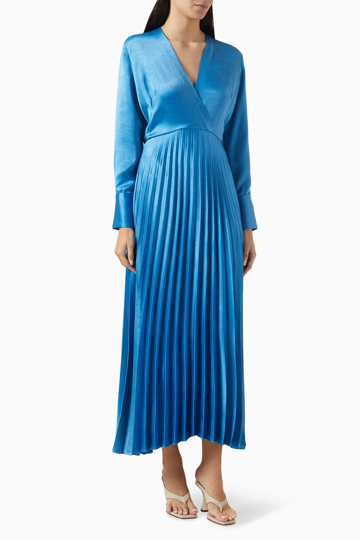 Woman wearing a vibrant blue pleated satin midi dress with long sleeves and V-neck, paired with beige heeled sandals — Sandro | Endless UAE