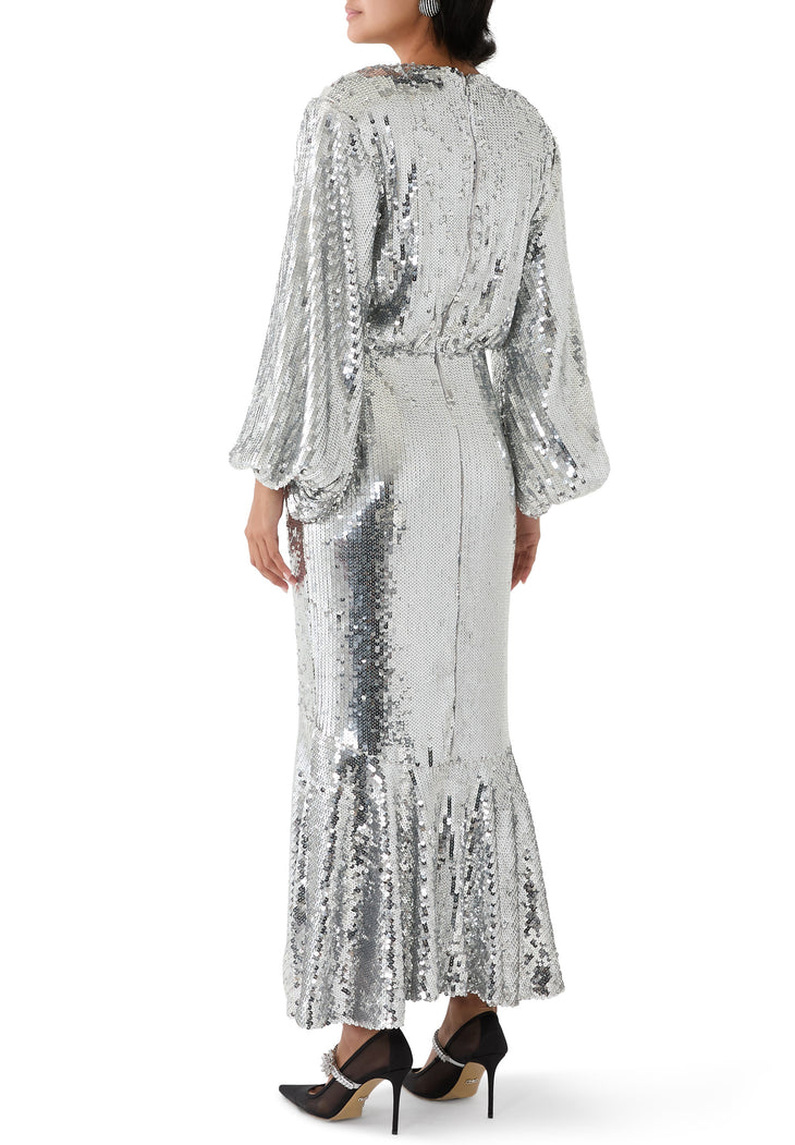 Silver sequined maxi dress with long balloon sleeves, fitted waist, and flared hem worn with black mesh heels — Rotate | Endless UAE