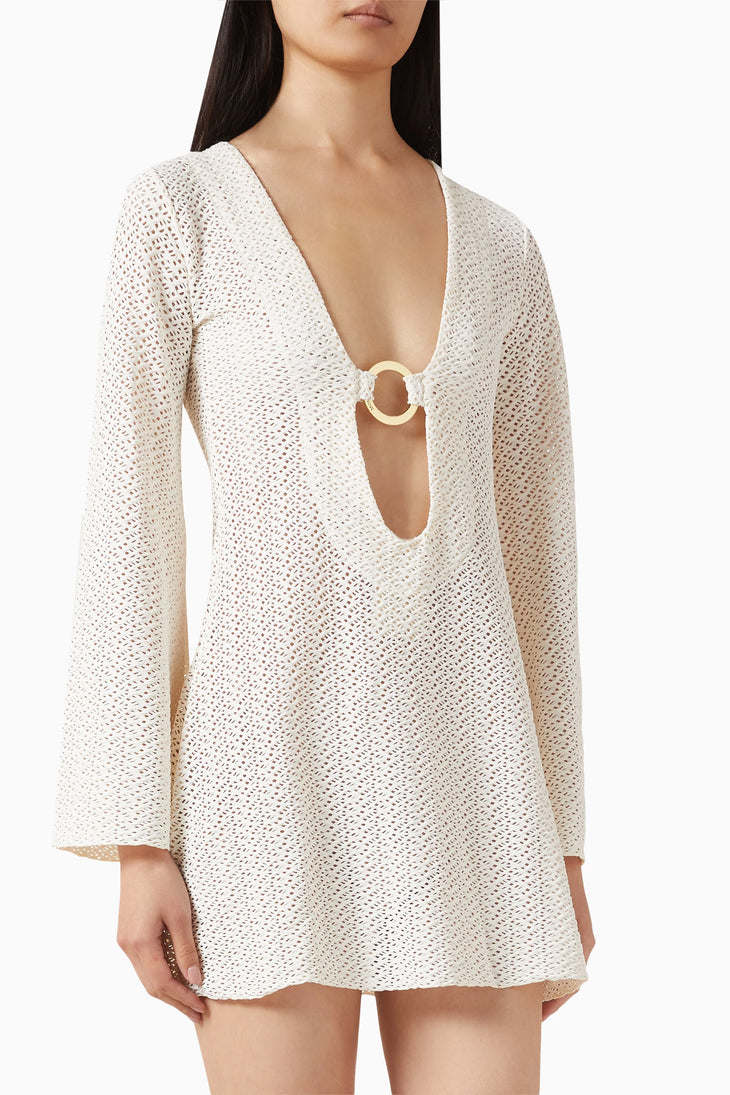 Woman wearing cream crochet mini dress with deep V-neckline and ring detail, long sleeves, semi-sheer knit fabric — Monday Swimwear | Endless UAE