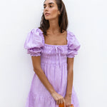 Lilac linen mini dress with puff sleeves and smocked bodice, styled with sunglasses and orange Fanta bottles — Else Adelia | Endless UAE