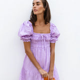 Lilac linen mini dress with puff sleeves and smocked bodice, styled with sunglasses and orange Fanta bottles — Else Adelia | Endless UAE