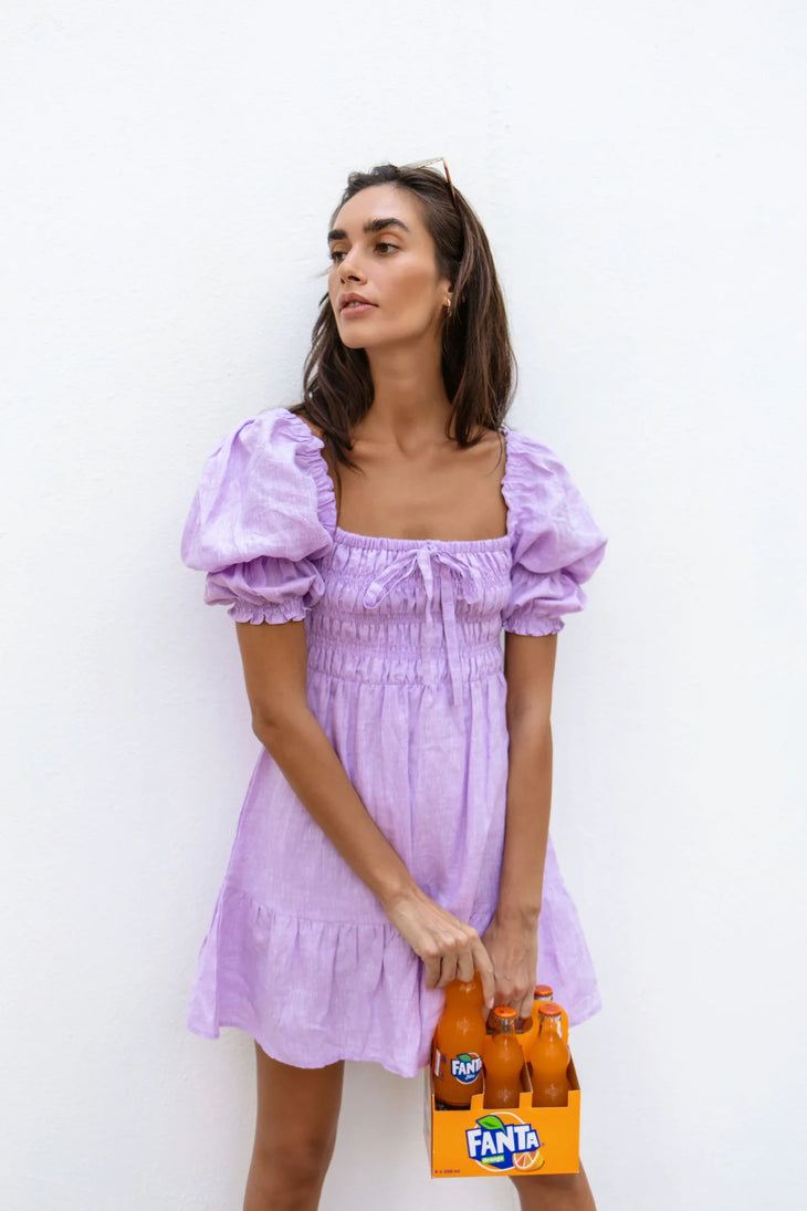 Lilac linen mini dress with puff sleeves and smocked bodice, styled with sunglasses and orange Fanta bottles — Else Adelia | Endless UAE