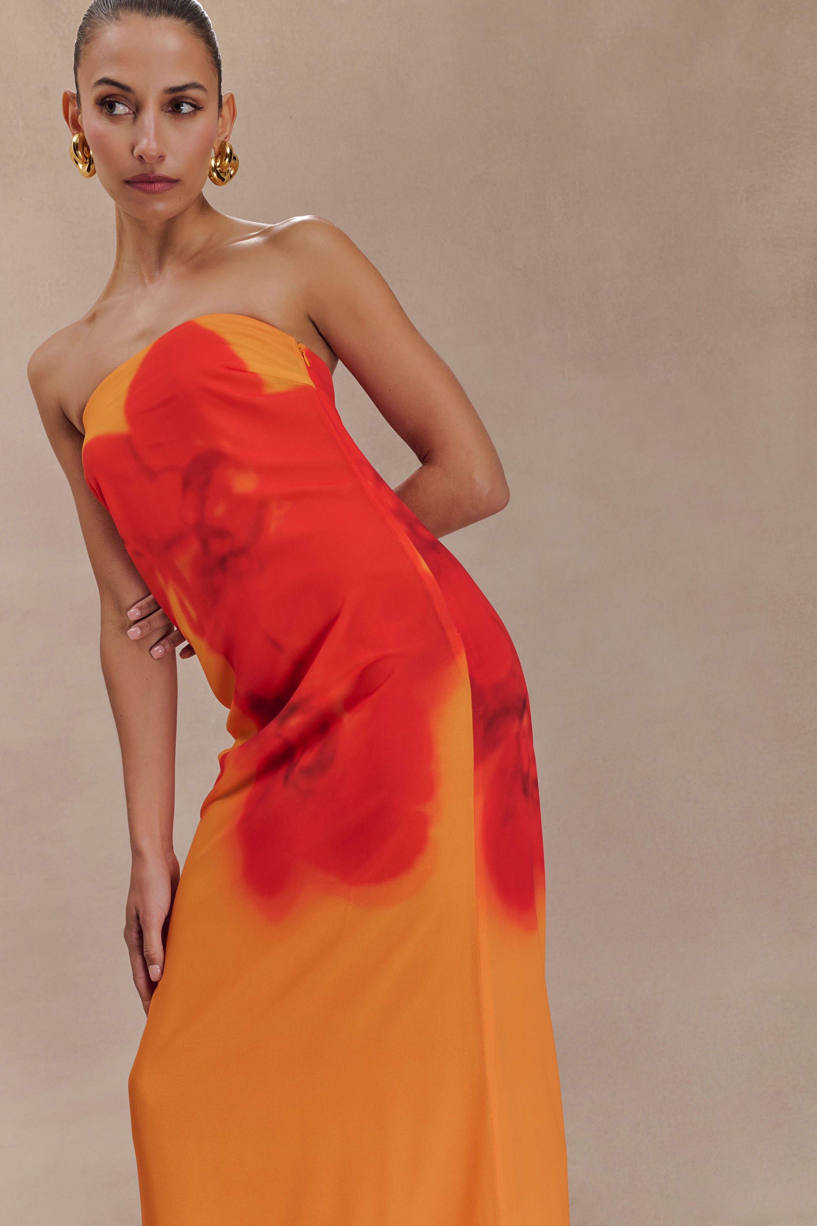 Woman wearing a strapless orange and red ombre chiffon maxi dress with gold hoop earrings — Meshki | Endless UAE