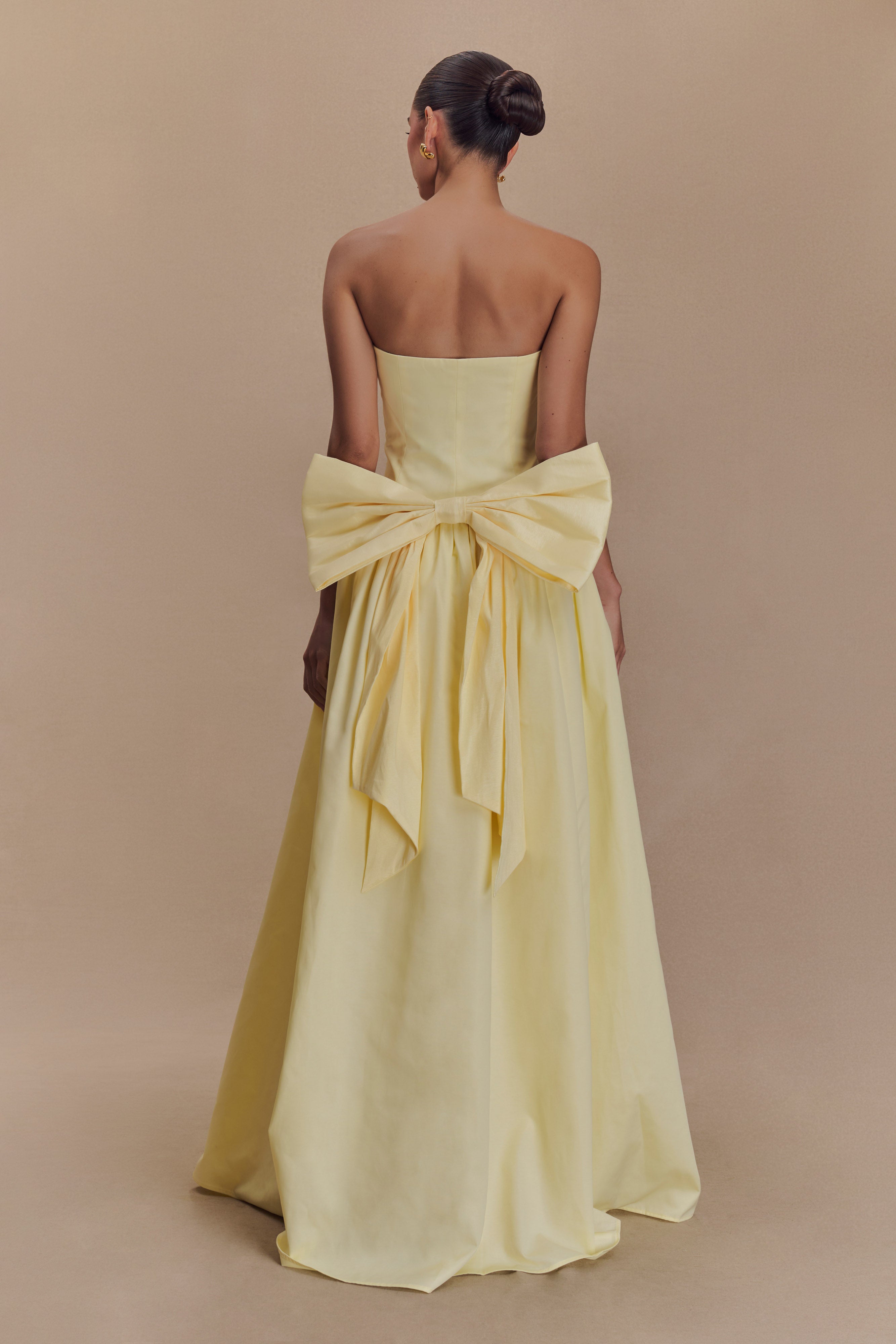 Elegant pale yellow strapless maxi dress with dramatic oversized bow detail at back, floor-length silhouette — Meshki | Endless UAE