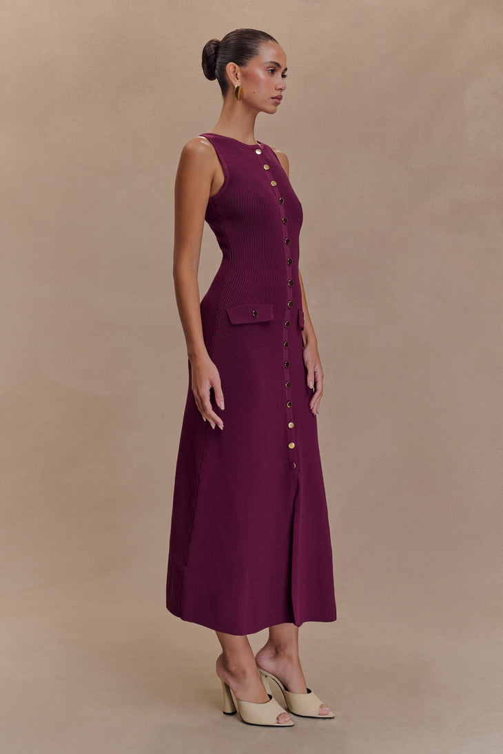Woman modeling burgundy sleeveless ribbed maxi dress with gold button detail and side pocket, paired with cream heels — Meshki | Endless UAE
