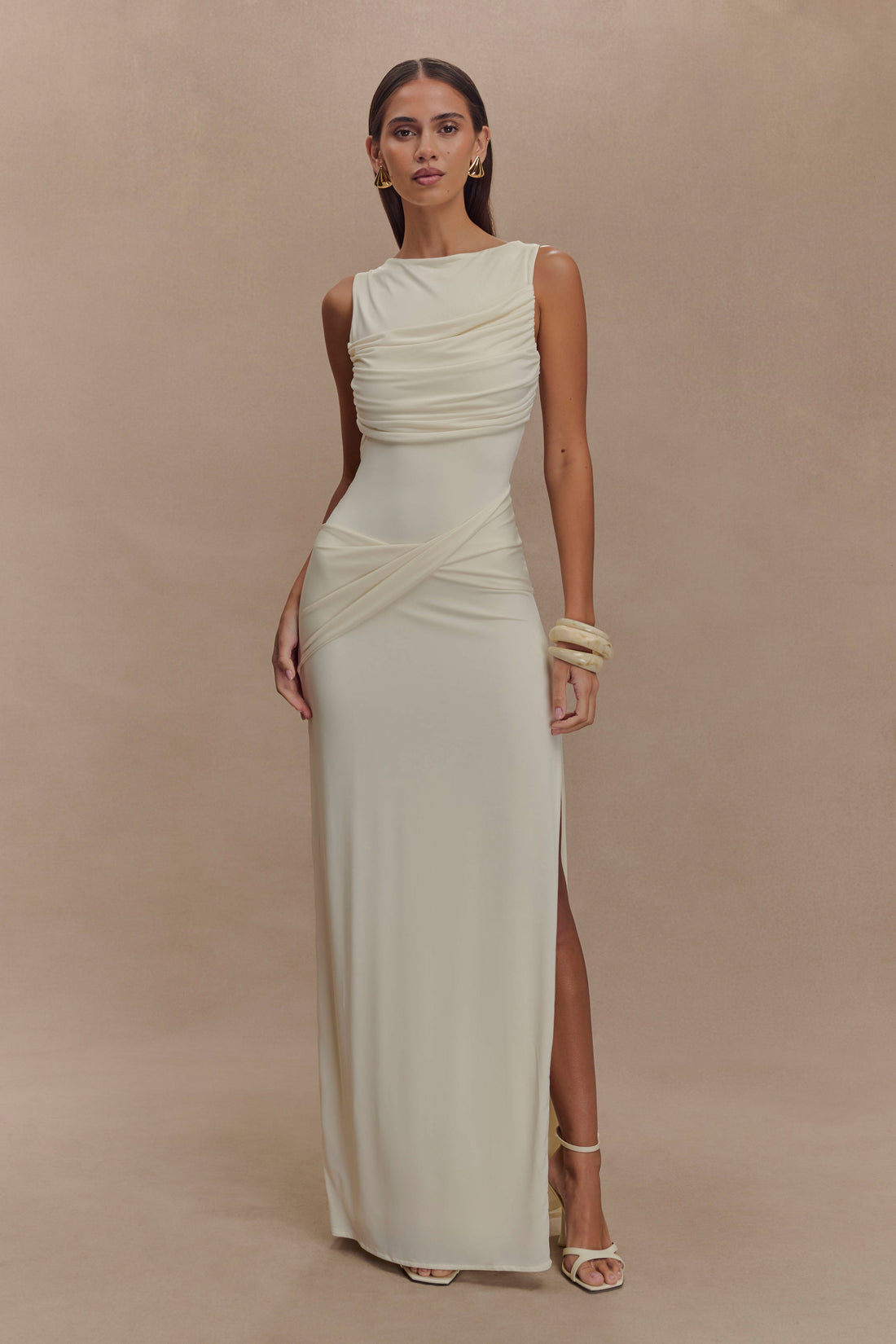 Elegant sleeveless cream maxi dress with ruched bodice draping and high leg slit, styled with gold accessories — Meshki | Endless UAE