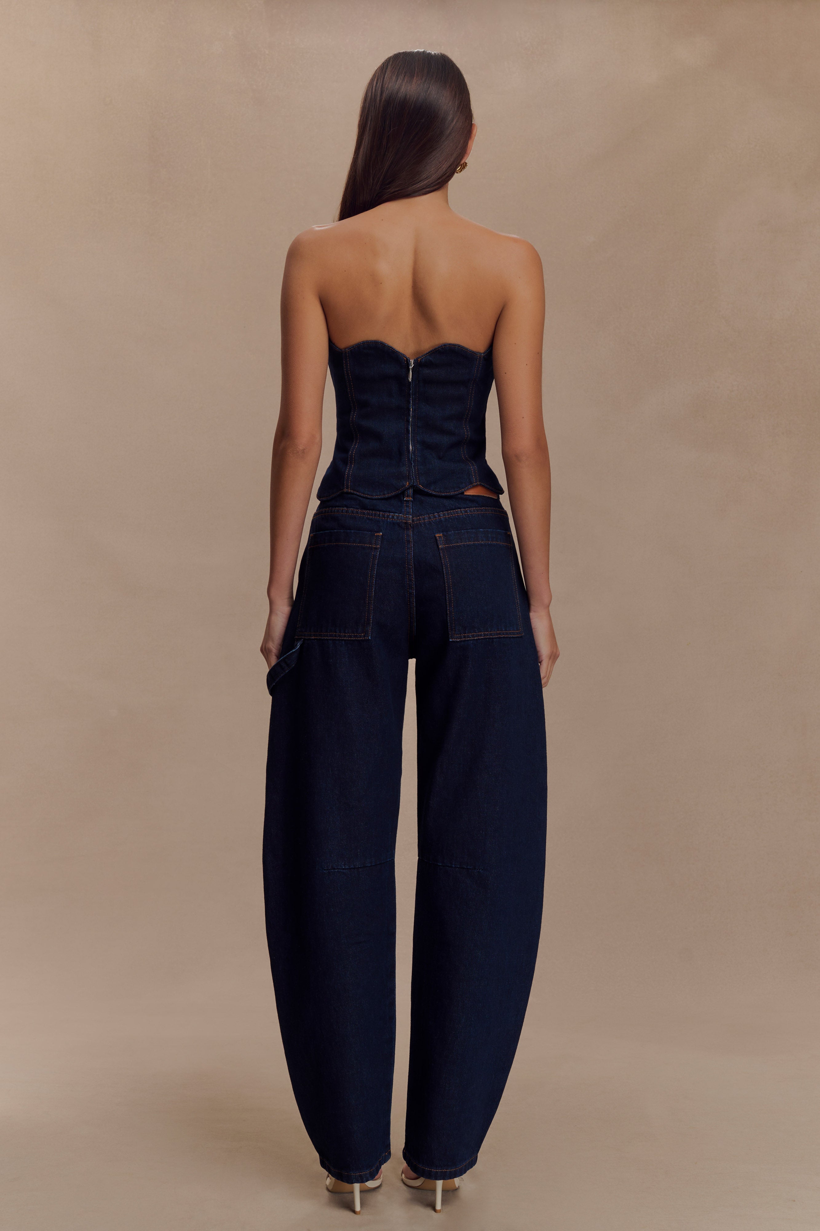 Rear view of woman wearing dark denim strapless corset top with zipper closure and matching wide-leg jeans — Meshki | Endless UAE
