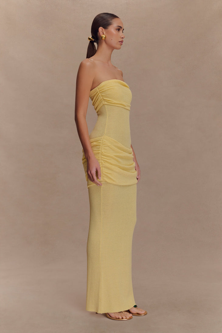 Woman wearing a yellow strapless knit maxi dress with ruched detailing, styled with gold earrings and sandals — Meshki | Endless UAE