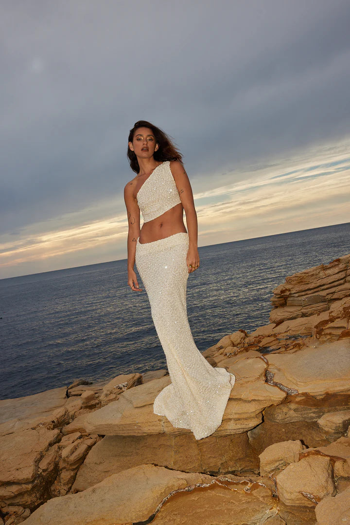 Elegant white sequin two-piece set with one-shoulder crop top and high-waist maxi skirt by ocean at sunset — Label Loft London | Endless UAE